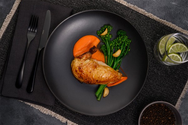 roast chicken breast with the skin on is served on a circular, graphite-colored plate along with a side of broccolini and a sweet potato puree