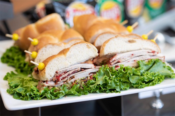 Roast pork sandwiches on deli rolls are served on a bed of lettuce on a square white plate.