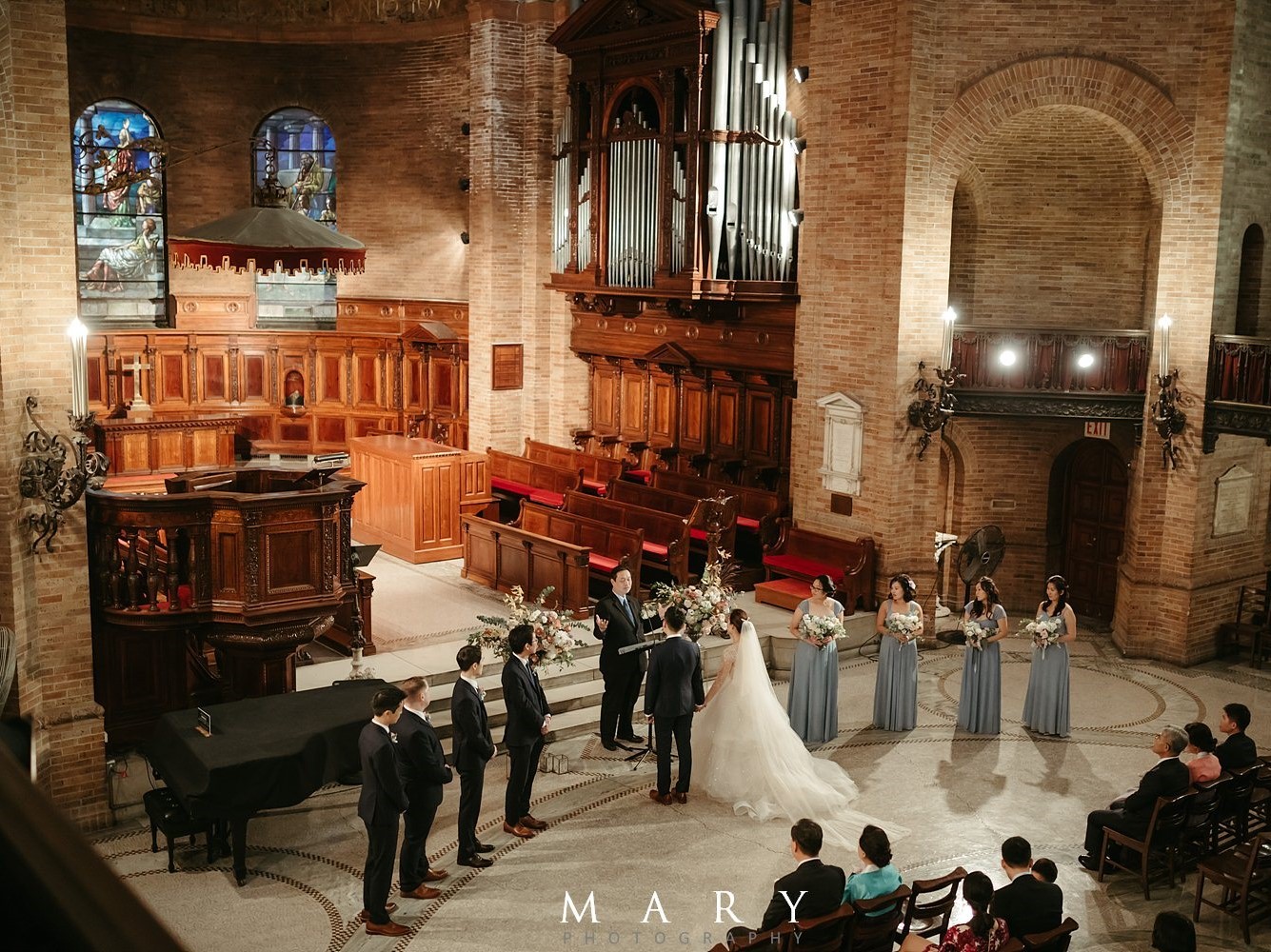 A couple surrounded on both sides by their groomsmen and bridesmaids as they are wed at Saint Paul's Chapel.
