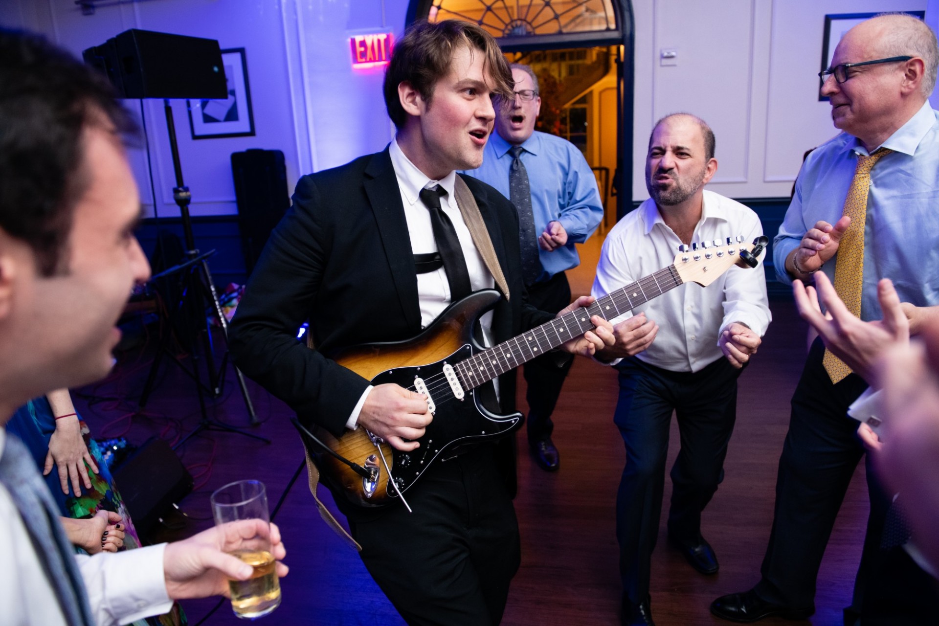 A guitarist stands on the Faculty House dance floor surrounded by party goers.