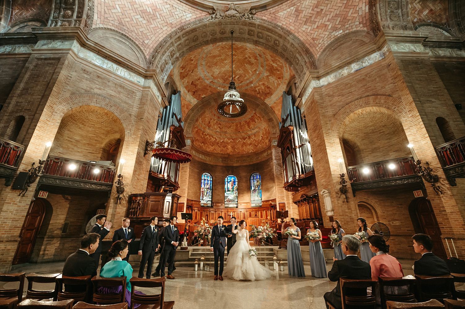 A bride and groom hold their hands up in triumph as they prepare to walk down the aisle in Saint Paul's Chapel together.