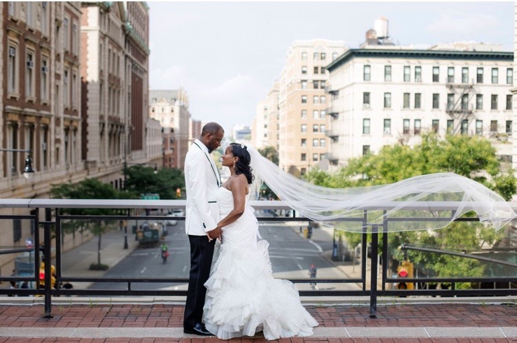 A couple, just married, embraces on Columbia University's campus, with city views in the background.